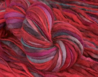 May include: A vibrant skein of hand-dyed yarn in shades of red, pink, and purple. The yarn is thick and textured, with a mix of colors creating a visually appealing effect. Ideal for knitting or crocheting projects.