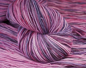 May include: A skein of yarn in shades of pink, purple, and white. The yarn is hand-dyed and has a variegated color pattern.