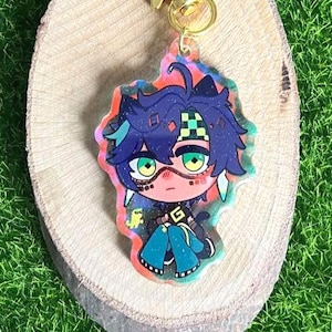 May include: A colorful anime-style keychain featuring a character with blue hair, green eyes, and a black outfit. The keychain has a gold star charm and is set on a wooden slice against a green background.