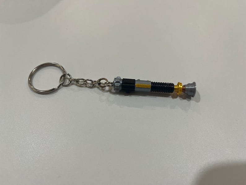 May include: A silver keychain with a black and silver lightsaber charm. The lightsaber has a gold accent.