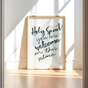 May include: A framed print with a white background and blue watercolour accents. The print features the text "Holy Spirit you are welcome in this place" in black calligraphy.