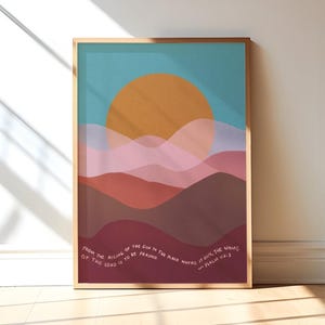 May include: A framed print featuring a colourful abstract landscape design with a large orange sun and layered pink, red and brown mountains. The print includes the text "From the rising of the sun to the place where it sets, the name of the Lord is to be praised - Psalm 113:3".