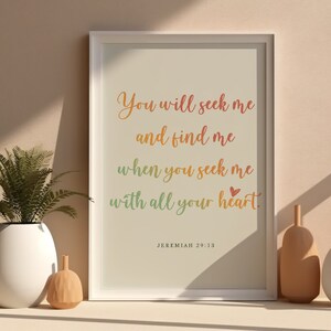 Puede incluir: Una impresión enmarcada con fondo blanco y un texto degradado arcoíris que dice "You will seek me and find me when you seek me with all your heart." El texto está en una fuente cursiva y hay un pequeño símbolo de corazón rojo al final del texto. La parte inferior de la impresión dice "JEREMIAH 29:13".