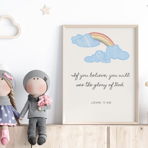 May include: A framed print featuring a rainbow and clouds, with the text "If you believe, you will see the glory of God. JOHN 11:40". Two dolls are sitting on a shelf in front of the print.