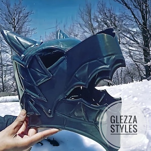 May include: A dark gray dragon-themed helmet with pointed ears and a detailed face. The helmet is held in a hand against a snowy background. The text "GLEZZA STYLES" is visible on the lower right side of the image.