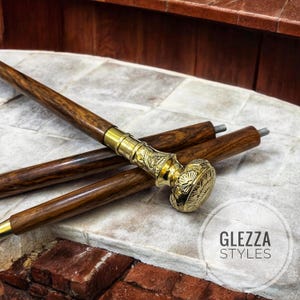 Könnte beinhalten: Ein Satz aus drei Gehstöcken aus Holz mit Messinggriffen. Die Griffe sind aufwendig mit floralen Mustern verziert. Die Stöcke sind braun und die Griffe sind golden.