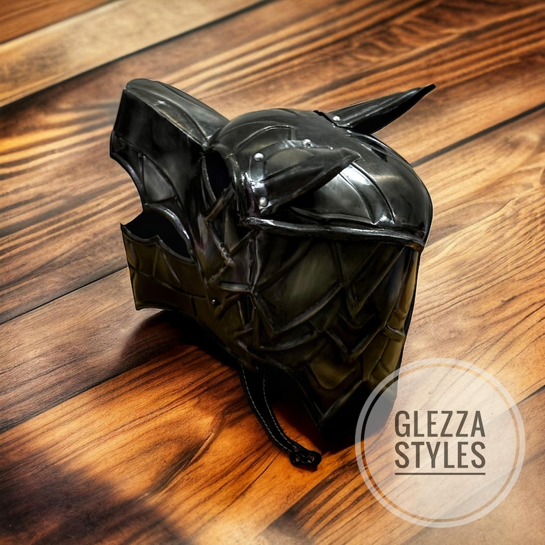 May include: A black, stylized helmet with a wolf-like design, featuring pointed ears and a horn. The helmet has a textured, metallic appearance and is secured with a chin strap. The text "GLEZZA STYLES" is visible.
