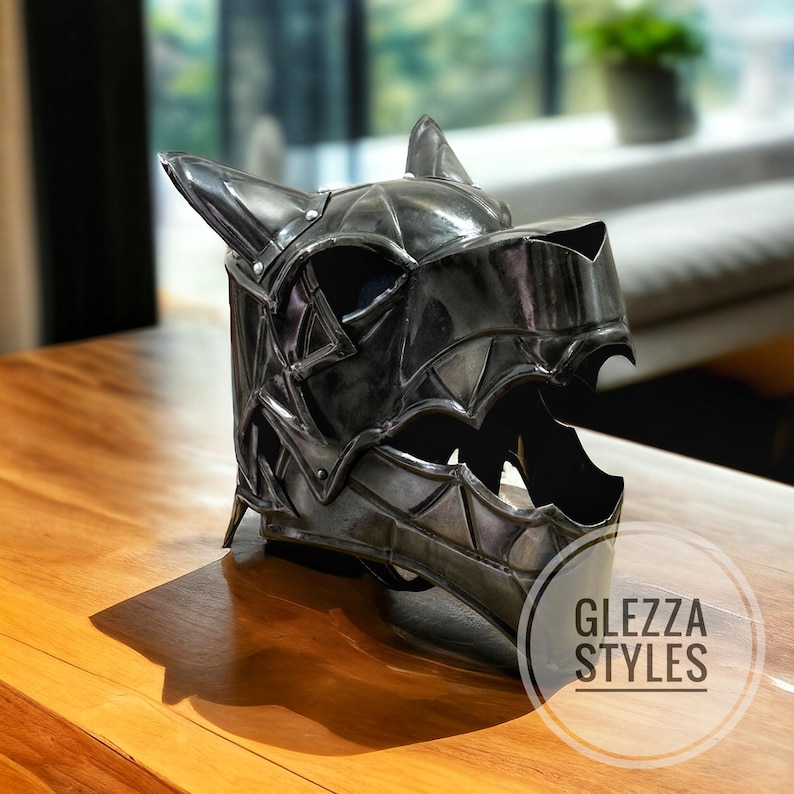 May include: A metallic gray helmet with a wolf-like design, featuring pointed ears and a jagged mouth opening. The helmet is detailed with geometric patterns and rivets. The logo "GLEZZA STYLES" is visible on the lower right.