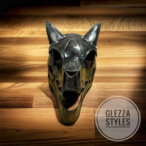 May include: A black, stylized cat mask with pointed ears and a wide open mouth. The mask has a metallic sheen and is decorated with small silver studs. The mask is displayed on a wooden surface. The text "GLEZZA STYLES" is in a circle in the bottom right corner.