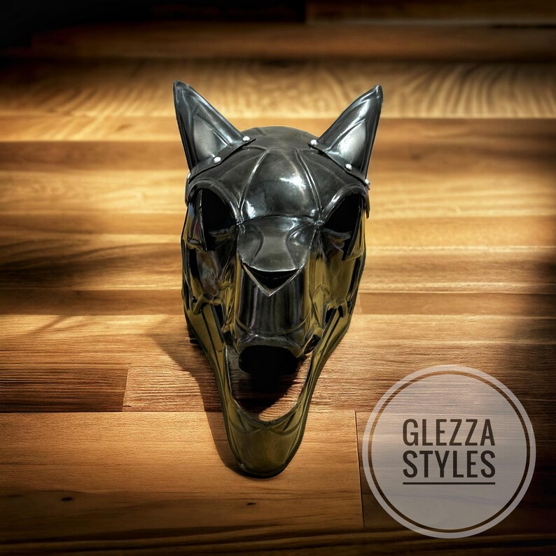 May include: A black, stylized cat mask with pointed ears and a wide open mouth. The mask has a metallic sheen and is decorated with small silver studs. The mask is displayed on a wooden surface. The text "GLEZZA STYLES" is in a circle in the bottom right corner.