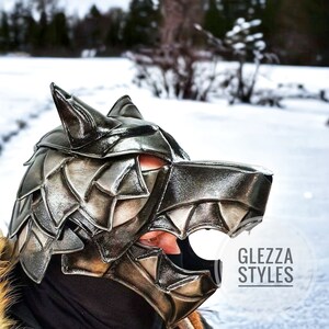 May include: A metallic silver wolf mask with a detailed, layered design. The mask covers the face and head, featuring pointed ears and an open mouth. The text "GLEZZA STYLES" is visible on the lower right. The background is a snowy landscape.