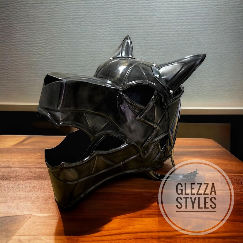 May include: A black, stylized helmet shaped like a wolf's head, with pointed ears and a detailed, geometric design. The helmet is made of a shiny material and sits on a wooden surface. The text "GLEZZA STYLES" is in a circle on the bottom right.