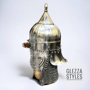 May include: A silver metal helmet with a pointed top and a rounded, ribbed crown. The helmet has a face guard, chainmail, and decorative metalwork. The text "GLEZZA STYLES" is visible on the right side.