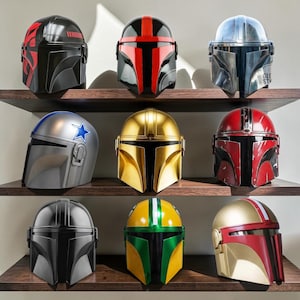 May include: Nine Mandalorian-style helmets displayed on three wooden shelves. The collection features various color schemes including black with red accents, metallic silver, gold, red with weathering, and green and yellow combinations.