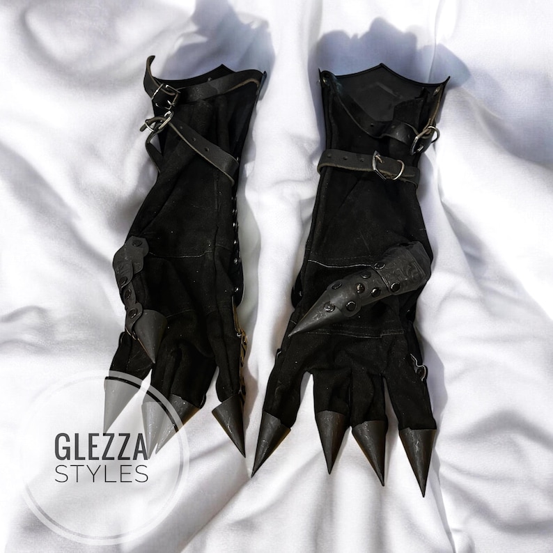 Op de afbeelding: Een paar zwarte handschoenen met puntige, kegelvormige vingerextensies en verstelbare leren riemen met metalen gespen bij de polsen. De handschoenen zijn versierd met kleine metalen studs en bevatten de tekst GLEZZA STYLES in de hoek.