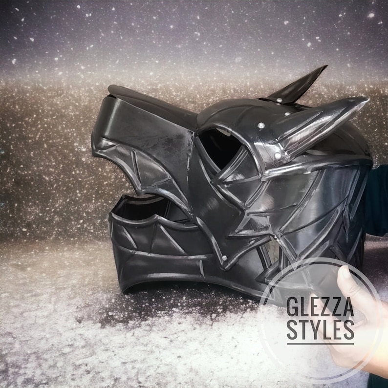 May include: A black, stylized helmet with pointed horns and intricate detailing. The helmet has a textured surface and is designed with angular shapes. The text "GLEZZA STYLES" is visible on the image.