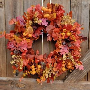 May include: A fall-themed wreath with red, orange, and yellow leaves, berries, and sprigs. The wreath is made of artificial materials and is perfect for decorating a door or wall.
