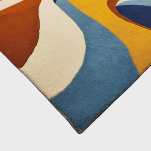 May include: A rectangular area rug featuring a bold pattern of large, sweeping curved shapes in vibrant colors including deep rust orange, creamy off-white, bright mustard yellow, and muted slate blue, with a dark blue circular accent.