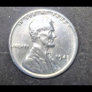 May include: A close-up of a silver 1943 Lincoln penny. The coin features a profile of Abraham Lincoln and the words "In God We Trust" and "Liberty". The year "1943" is visible.