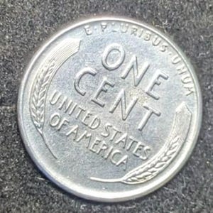 May include: A silver United States one-cent coin. The coin features the words "ONE CENT" in large capital letters, with "UNITED STATES OF AMERICA" below. The coin is surrounded by the words "E PLURIBUS UNUM" and wheat stalks.