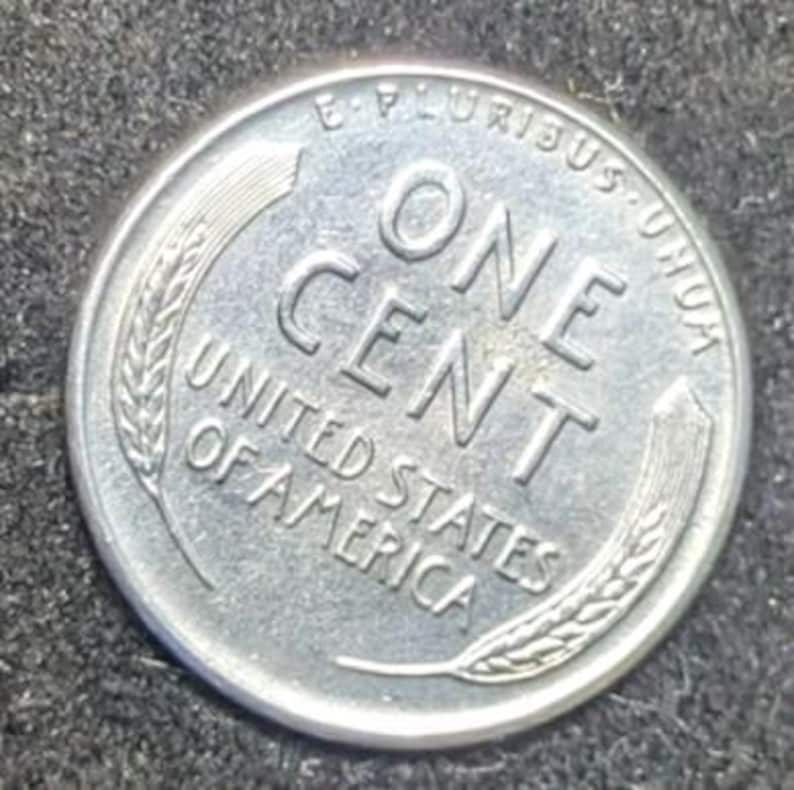 May include: A silver United States one-cent coin. The coin features the words "ONE CENT" in large capital letters, with "UNITED STATES OF AMERICA" below. The coin is surrounded by the words "E PLURIBUS UNUM" and wheat stalks.