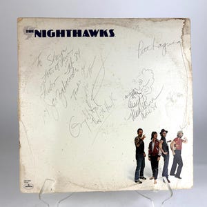 Puede incluir: Funda de álbum de vinilo vintage para "The Nighthawks" con la imagen de los miembros de la banda y firmas. La funda del álbum es blanquecina con el nombre de la banda en azul. Firmas y un dibujo en tinta negra.