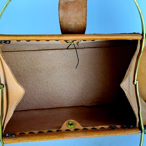 May include: Open view of a tan leather handbag with a brass handle and a leather strap. The bag is stitched with black thread and has a brass clasp. The interior is a lighter tan color.