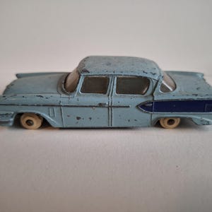 Könnte beinhalten: Ein hellblaues Spielzeugauto aus Druckguss mit dunkelblauen Akzenten an der Seite. Das Spielzeugauto hat weiße Räder und weist Gebrauchsspuren auf, was auf ein antikes Sammlerstück hindeutet.