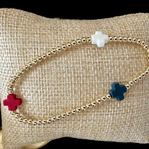 May include: A gold beaded bracelet with red, white and blue cross charms.
