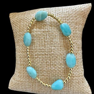May include: A bracelet with light blue oval-shaped stones and gold beads.
