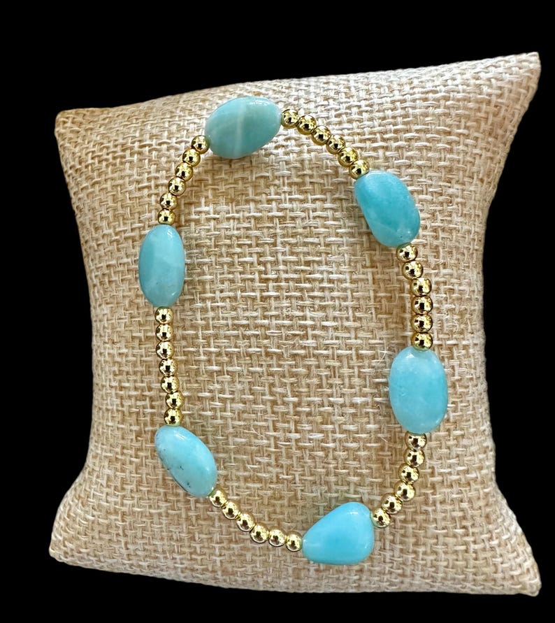 May include: A bracelet with light blue oval-shaped stones and gold beads.