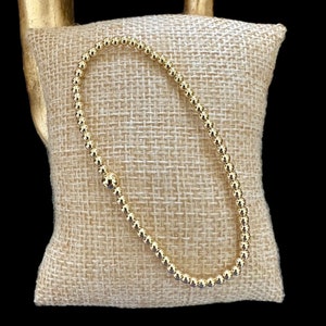 May include: A gold beaded bracelet with a smooth, polished finish. The bracelet is made of small, round beads that are strung together to create a delicate and elegant look.