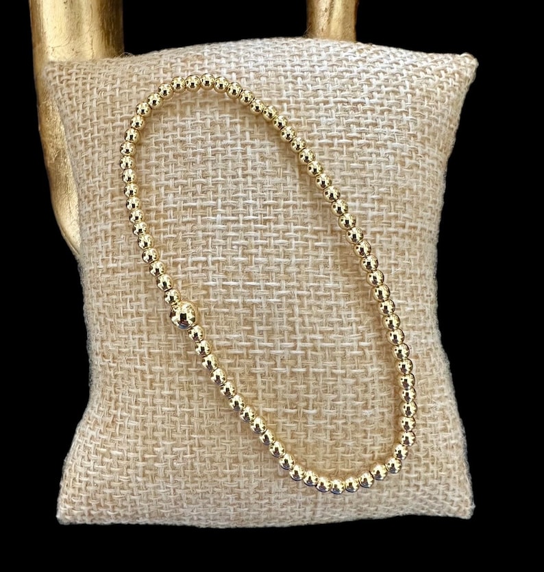 May include: A gold beaded bracelet with a smooth, polished finish. The bracelet is made of small, round beads that are strung together to create a delicate and elegant look.
