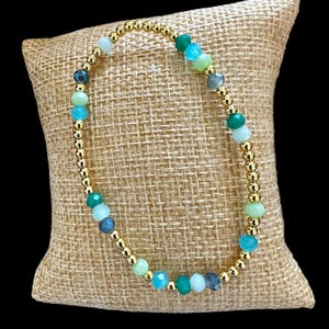 May include: A gold beaded bracelet with green, blue, and gray gemstone beads.