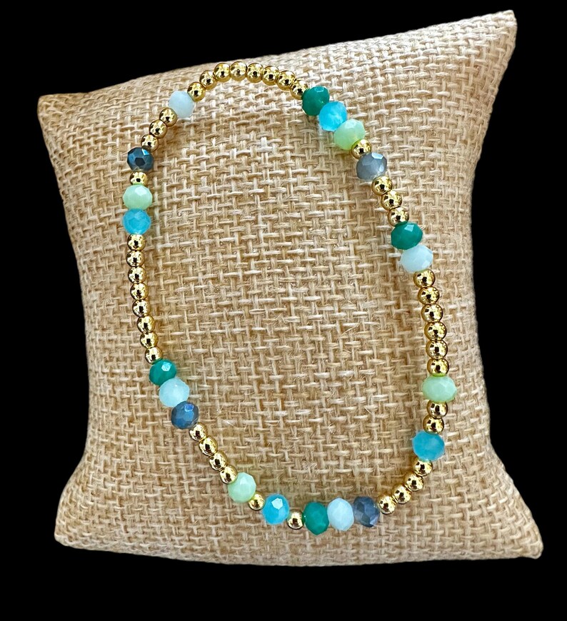 May include: A gold beaded bracelet with green, blue, and gray gemstone beads.