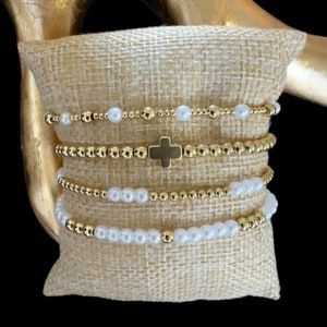 May include: A set of four gold bead bracelets with a small gold cross charm. Two of the bracelets are made with white pearls.
