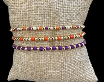 Pulseras de fútbol apilables de color morado y naranja chapadas en oro con colores personalizables.