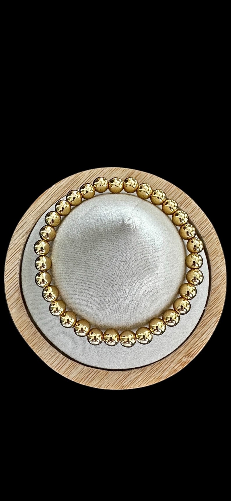 May include: A gold beaded bracelet with a shiny finish. The bracelet is displayed on a wooden stand.
