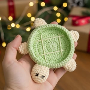 Könnte beinhalten: Gehäkelter Schildkröten-Untersetzer in Hellgrün und Creme. Die Schildkröte hat ein Tic-Tac-Toe-Gitter auf dem Rücken und gestickte Augen. Geeignet als Dekoration oder Geschenk.