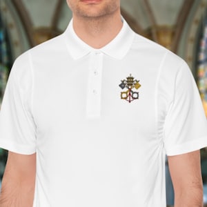 Könnte beinhalten: Weißes Poloshirt mit einem kleinen Emblem auf der linken Brust. Das Emblem hat ein detailliertes Design mit goldenen, roten und blauen Akzenten. Das Shirt hat einen klassischen Kragen und eine Knopfleiste.