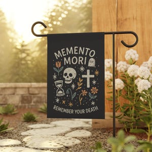 May include: Black garden flag with the words "MEMENTO MORI REMEMBER YOUR DEATH" in white. The flag features a skull, hourglass, cross, flowers, and stars. The flag is displayed on a black metal garden stake.