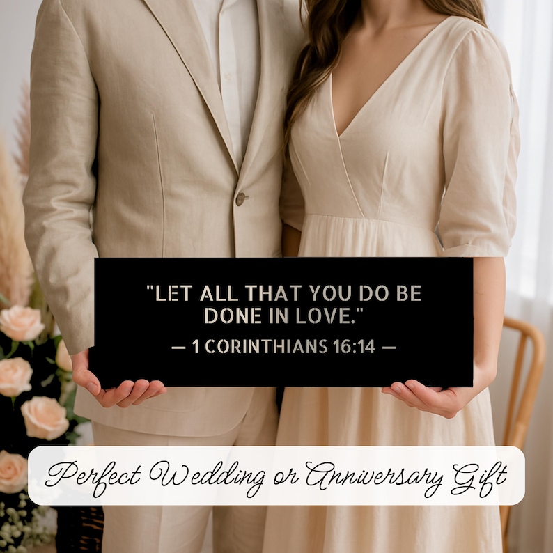 Op de afbeelding: Een zwart rechthoekig bord met de tekst "LET ALL THAT YOU DO BE DONE IN LOVE." - 1 CORINTHIANS 16:14 -" vastgehouden door een stel. Het bord bevat ook de tekst "Perfect Wedding or Anniversary Gift". Het paar draagt formele kleding.