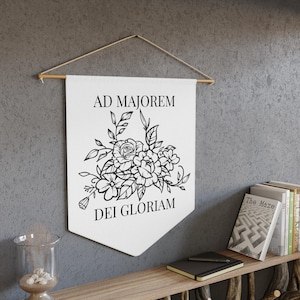 May include: A white canvas banner with black text and a floral design. The text reads "Ad Majorem Dei Gloriam".