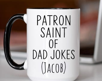 May include: White ceramic mug with a black handle and rim. The mug features the text "PATRON SAINT OF DAD JOKES (JACOB)" in black, bold letters. The mug is designed for coffee, tea, or any beverage.