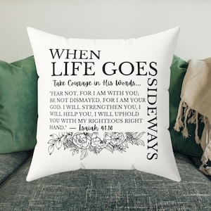 Könnte beinhalten: Weißes Kissen mit schwarzem Text: "WHEN LIFE GOES SIDEWAYS" und ein Zitat aus Jesaja 41,10. Das Kissen hat unten ein Blumendesign.