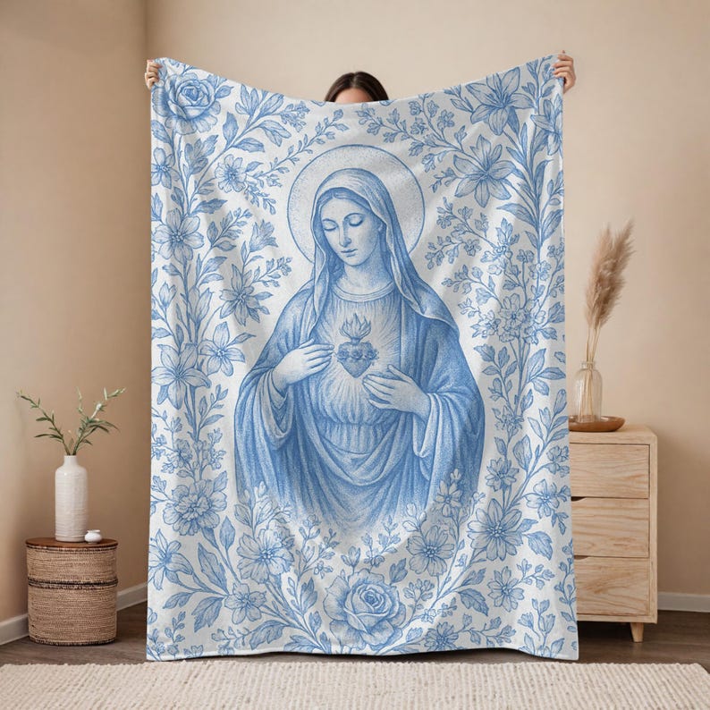 May include: Blue and white throw blanket featuring a floral design and a central image of the Virgin Mary holding a heart.