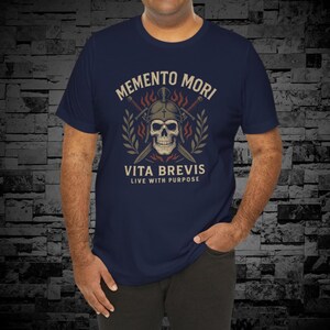 Puede incluir: Camiseta azul marino con un dise&ntilde;o vintage que presenta una calavera con casco, espadas cruzadas y el texto "MEMENTO MORI VITA BREVIS LIVE WITH PURPOSE". El dise&ntilde;o incluye llamas y ramas de laurel.