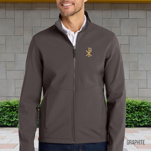 Può includere: Giacca softshell color grafite con cerniera a tutta lunghezza e collo alto. La giacca presenta un emblema ricamato dorato sul petto sinistro. La parola "GRAPHITE" è stampata in bianco in basso a destra.