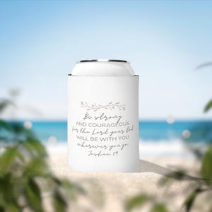 May include: White can cooler with a floral design and the text "Be strong and courageous for the Lord your God will be with you wherever you go. Joshua 1.9"