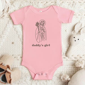 May include: Pink baby onesie with a black line drawing of a person holding a flower and the text "daddy's girl".